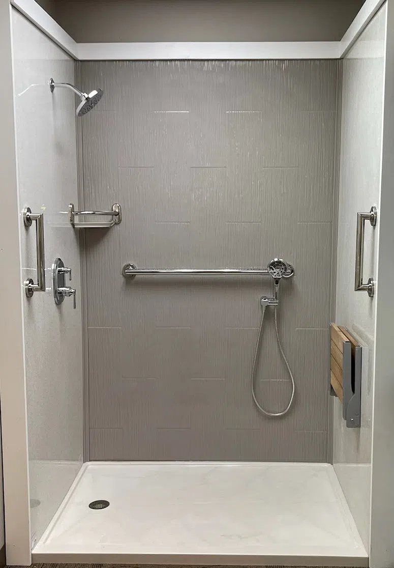 Groutless shower with gray wall panels, grab bars and a handheld shower head, available at Sidney Kitchen and Bath in Winchester, VA