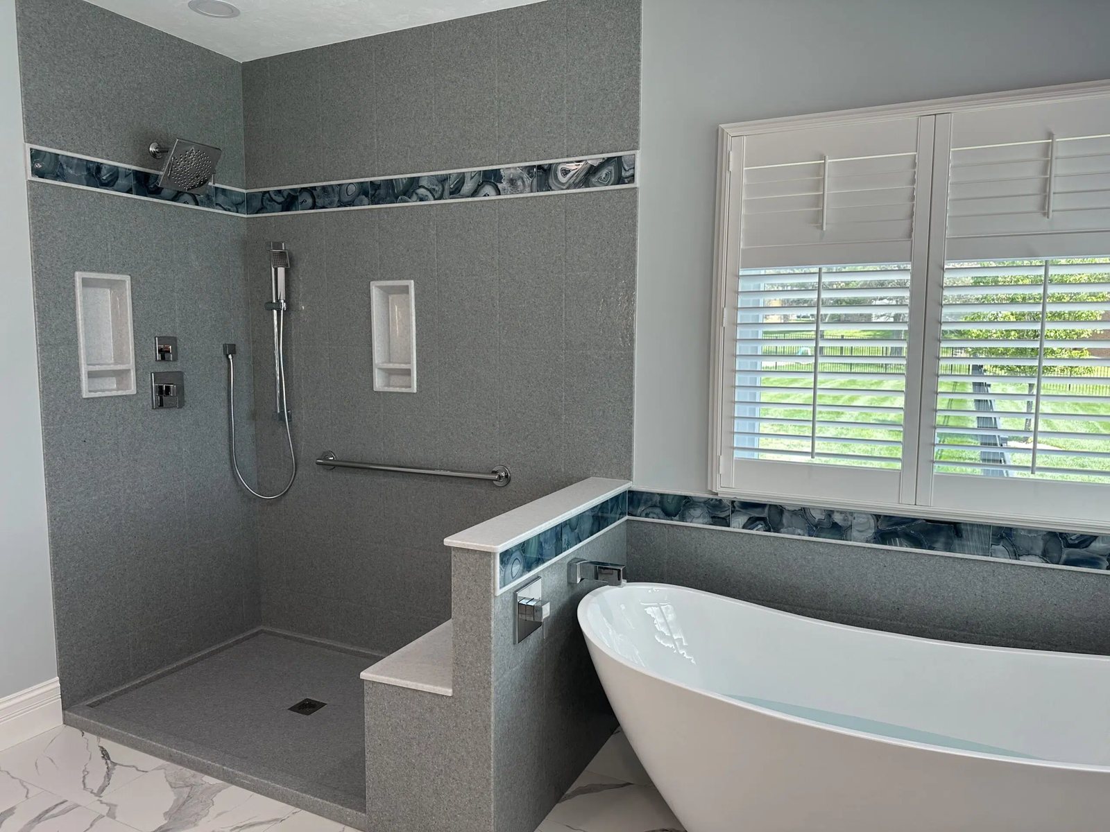 Walk in groutless shower with a mosaic accent band beside a freestanding tub, available at Sidney Kitchen and Bath in Winchester, VA