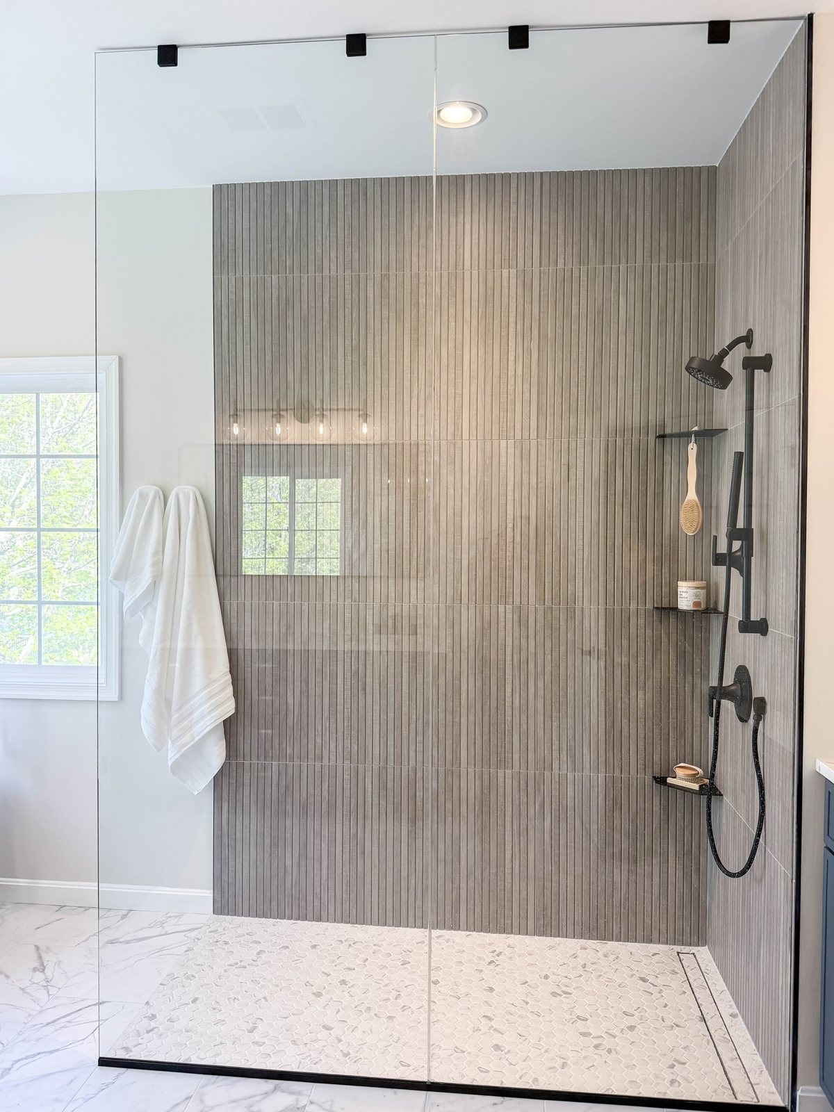 Walk in shower with large format wall tile and a glass panel in a Winchester, VA bathroom finished by Sidney Design and Build